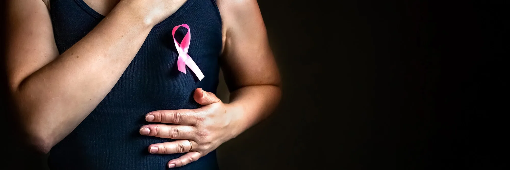 A woman has a pink ribbon on her chest, in support of breast cancer patients. Banner